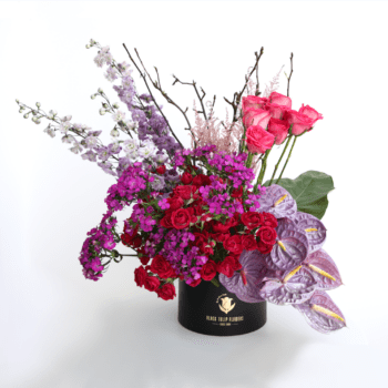 A vibrant arrangement of seasonal flowers in purple, red, and fuchsia, presented in a stylish box.
