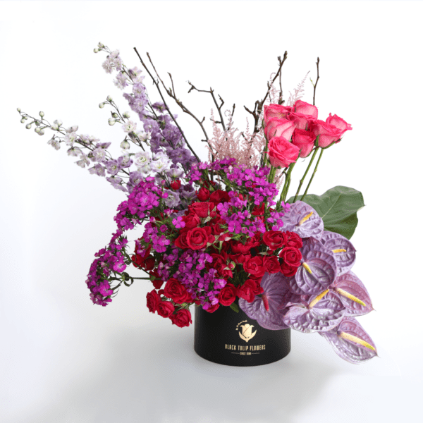 A vibrant arrangement of seasonal flowers in purple, red, and fuchsia, presented in a stylish box.
