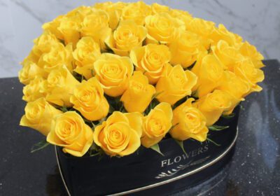 A box filled with vibrant yellow heart-shaped roses, elegantly arranged for a cheerful floral display.