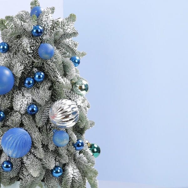 2 (265) A small, frosted Christmas tree decorated with blue and silver ornaments. The tree is in a white pot and sits on a blue background.