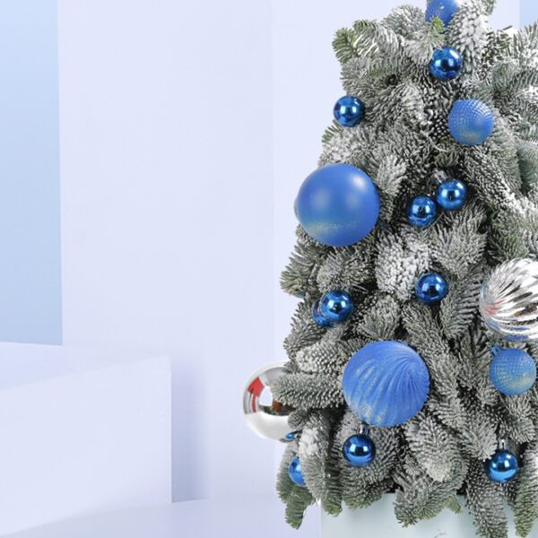 A small, frosted Christmas tree decorated with blue and silver ornaments. The tree is in a white pot and sits on a blue background.