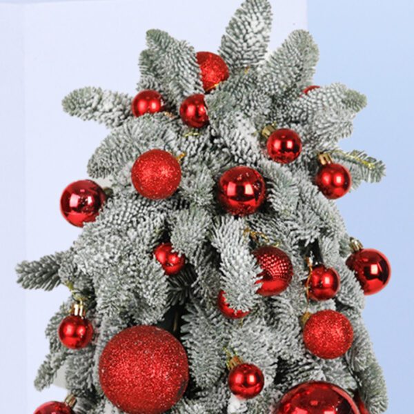 A small, frosted Christmas tree decorated with red ornaments. The tree is in a black pot and sits on a blue background.