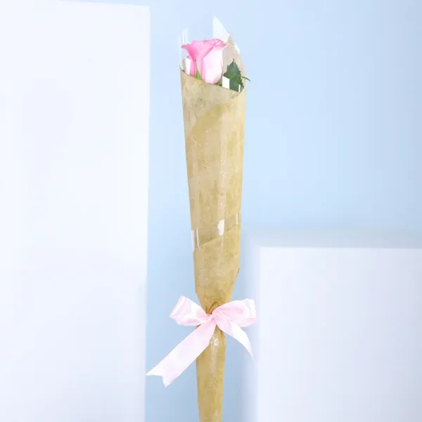 01-41 A single pink rose elegantly wrapped in delicate paper, showcasing its soft petals and green stem.