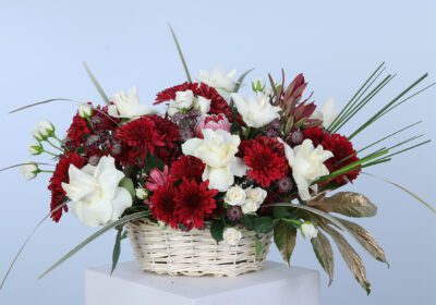 Basket arrangement of red chrysanthemums and white roses with lush greenery for a stunning floral display.
