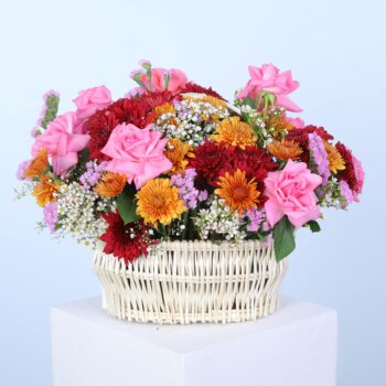 A vibrant basket filled with colourful mix of flowers displayed elegantly on a white pedestal against a neutral background.