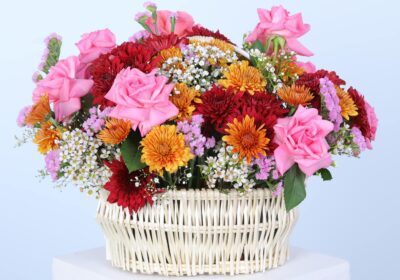 A vibrant basket filled with colourful mix of flowers displayed elegantly on a white pedestal against a neutral background.
