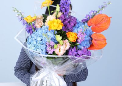 Stunning bouquet with hydrangeas, Anthurium, peach Lisianthus, roses, Mathiola, and Delphinium, elegantly wrapped in glass sheet.