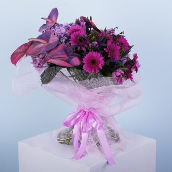 A bouquet of pink anthurium, hydrangea, gerbera daisies, and other flowers wrapped in a pink mesh with a pink ribbon.