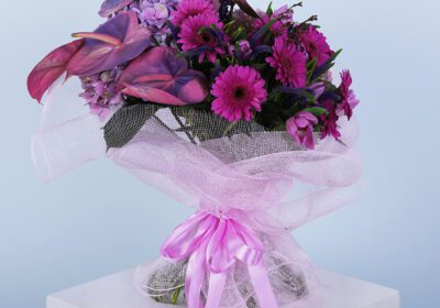 A bouquet of pink anthurium, hydrangea, gerbera daisies, and other flowers wrapped in a pink mesh with a pink ribbon.