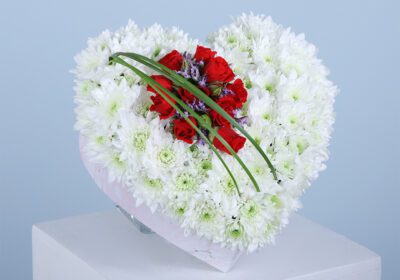 A heart-shaped floral arrangement with white and red flowers.