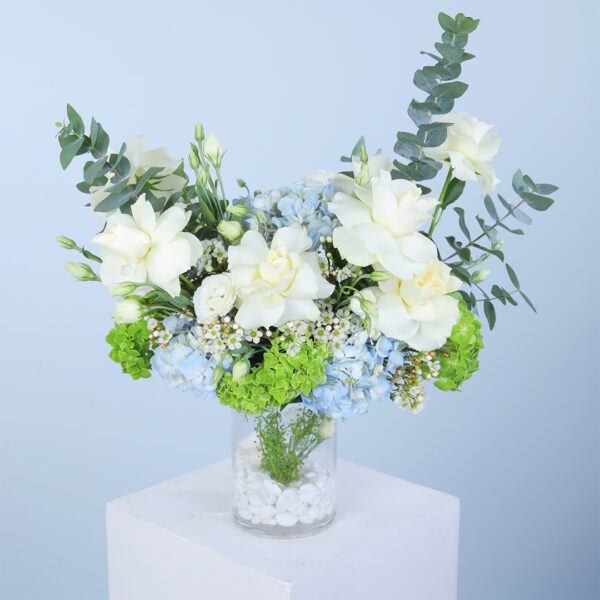 A glass vase filled with white roses, blue and green hydrangeas, and lisianthus, accented by eucalyptus.