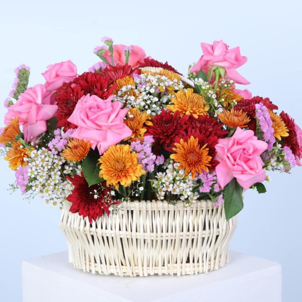 A lively basket filled with a mix of colourful flowers, beautifully presented on a white pedestal.