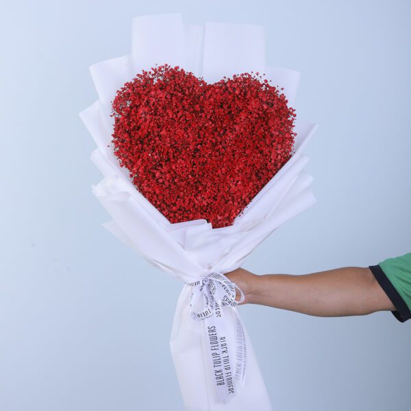 A heart-shaped bouquet made of red gypsophila flowers, wrapped in white paper tied with white ribbon