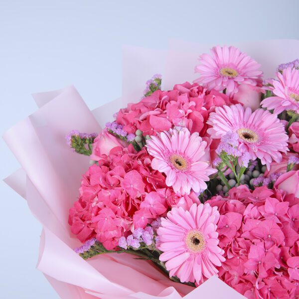 Colorful floral arrangement featuring pink gerberas, hydrangeas, roses, and ferns, wrapped in pink tissue paper.