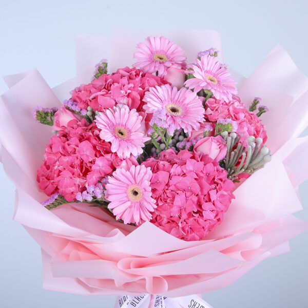 A stunning bouquet of mixed pink flowers, including gerberas, hydrangeas, and roses, with ferns and tied with a white ribbon.