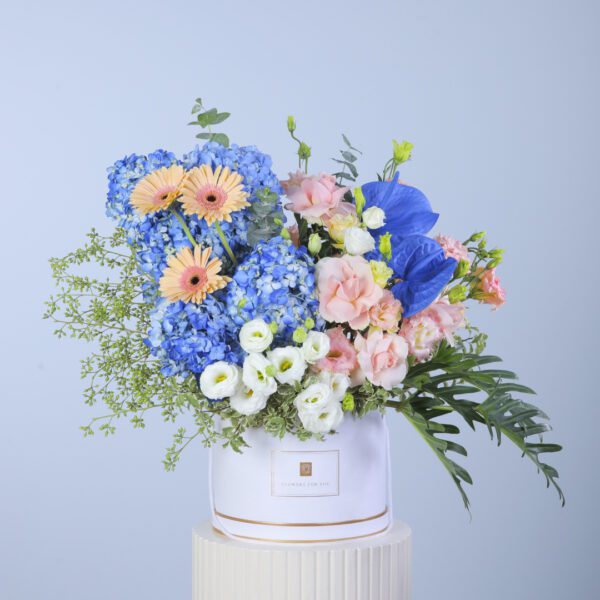 Beautiful arrangement of blue hydrangeas, daisies, and peach and white carnations in a white box with greenery.