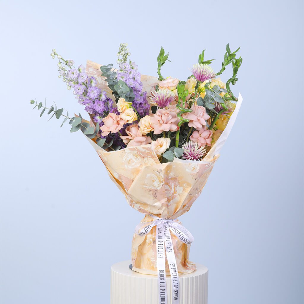 A beautiful bouquet featuring peach roses, delphinium, and lush greenery in an elegant arrangement.