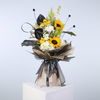 A bouquet featuring bright sunflowers and deep black leaves, artistically arranged on a pedestal for a striking effec