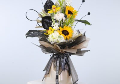 A bouquet featuring bright sunflowers and deep black leaves, artistically arranged on a pedestal for a striking effec