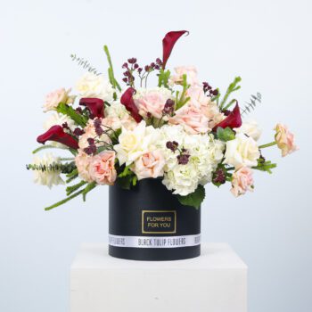 A black hat box filled with peach roses and white hydrangeas creates a stunning and elegant floral arrangement.