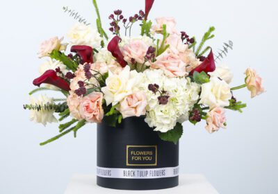 A black hat box filled with peach roses and white hydrangeas creates a stunning and elegant floral arrangement.
