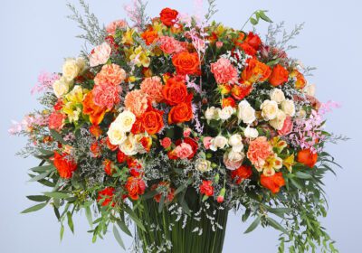 Floral arrangement with mix of flowers like carnations, garden roses, dianthus, buttercups,in shades of orange, pink, and cream in a vase