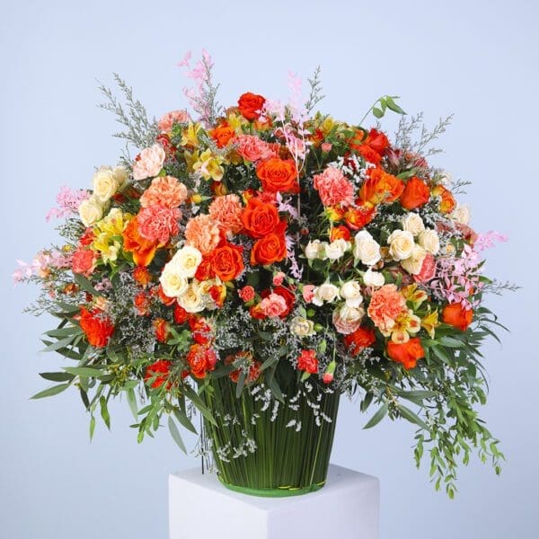 Floral arrangement with mix of flowers like carnations, garden roses, dianthus, buttercups,in shades of orange, pink, and cream in a vase