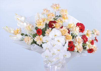 A vibrant bouquet with peach roses, white anthurium, phalaenopsis orchids, red gerberas, and greenery.