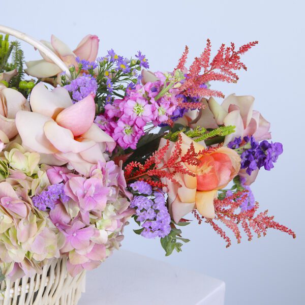 A charming basket brimming with pastel flowers like hydrangeas, roses, and carnations, complemented by fresh greenery.