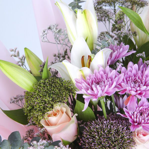 A stunning arrangement of mixed blooms wrapped in a soft pink floral wrap, exuding elegance and grace.