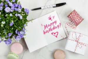 This image shows a birthday card with the message "Happy Birthday!" written in pink cursive. The card is surrounded by various birthday-themed items,