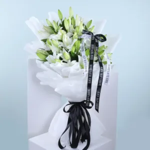 A bouquet of white lilies wrapped in white tissue paper with black ribbons and the words "Black Tulip Flowers" written on them.