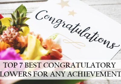 A colorful bouquet of flowers is placed on a wooden table, with a white card reading "Congratulations" lying on top. The text "TOP 7 BEST CONGRATULATORY FLOWERS FOR ANY ACHIEVEMENT" is superimposed over the image.