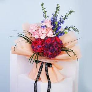 The image shows a beautiful bouquet of flowers arranged in a peach-colored wrapping paper. The bouquet features a mix of vibrant colors, including