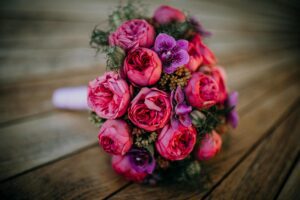 A vibrant bouquet of pink peonies and purple orchids rests on a wooden table.