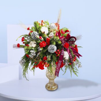 Red roses, pinecones, evergreens, and cotton stems in a golden transparent vase