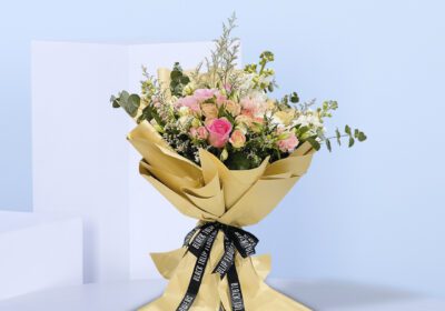 A bouquet of peach and pink roses in a light brown wrap tied with a black ribbon.