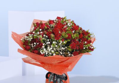 A bouquet of 20 red baby roses with added greenery and gypso wrapped in red paper and tied with black ribbon.
