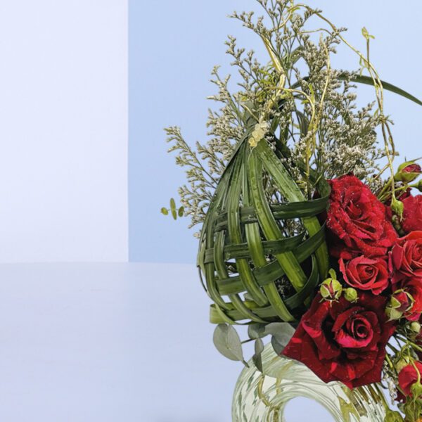 Unique floral arrangement with woven green accents, red roses, and tulips in a glass vase for decor or gifting purposes.