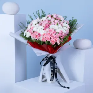 The image shows a beautiful bouquet of pink and white roses. The roses are arranged in a large, round shape and wrapped in white paper with a red stripe.