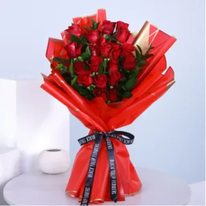 The image shows a beautiful bouquet of red roses wrapped in red paper. The bouquet is tied with a black ribbon