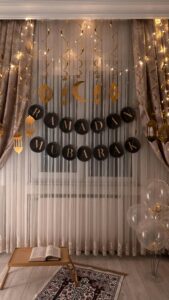 A decorated room, likely for Ramadan celebrations, featuring a "Ramadan Mubarak" banner, lights, curtains, and other festive elements.