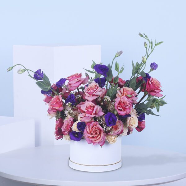 Pink and purple flowers arranged in a stylish white floral box.