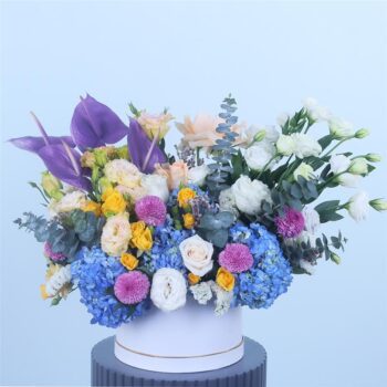 Elegant blue, white, and purple floral arrangement in a chic round box.