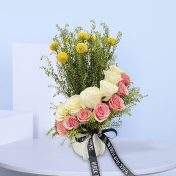 A vase with pink and white roses, yellow billy balls, and greenery.