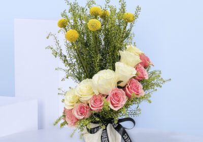 A vase with pink and white roses, yellow billy balls, and greenery.