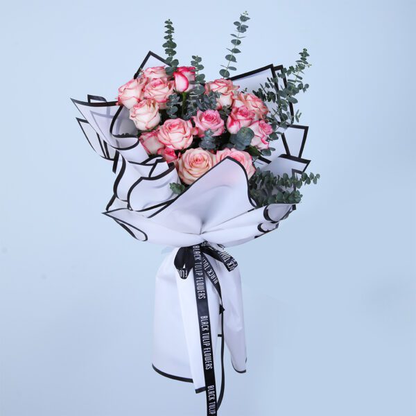 Hand bouquet of blush pink and peach roses with eucalyptus, wrapped in white and black paper.