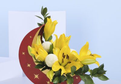Crescent-shaped arrangement with yellow lilies, white chrysanthemums, and green leaves.
