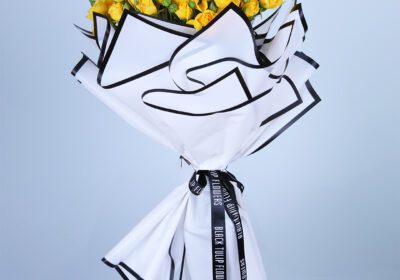 Hand bouquet of fresh yellow flowers wrapped in stylish white and black paper.
