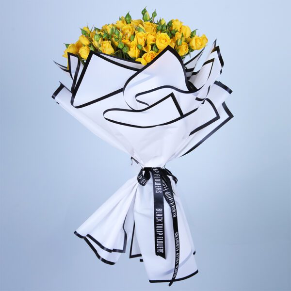 Hand bouquet of fresh yellow flowers wrapped in stylish white and black paper.